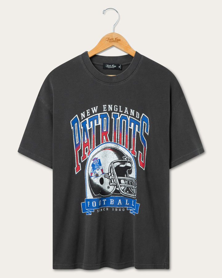 A dark gray short-sleeve t-shirt hanging on a wooden hanger against a light beige background. The shirt features a large graphic print of the New England Patriots football helmet and logo with the words 'NEW ENGLAND PATRIOTS FOOTBALL' in red, white, and blue.